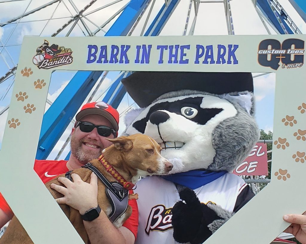 Man with dog and mascot at Bark in the Park event, promoting custom tees.