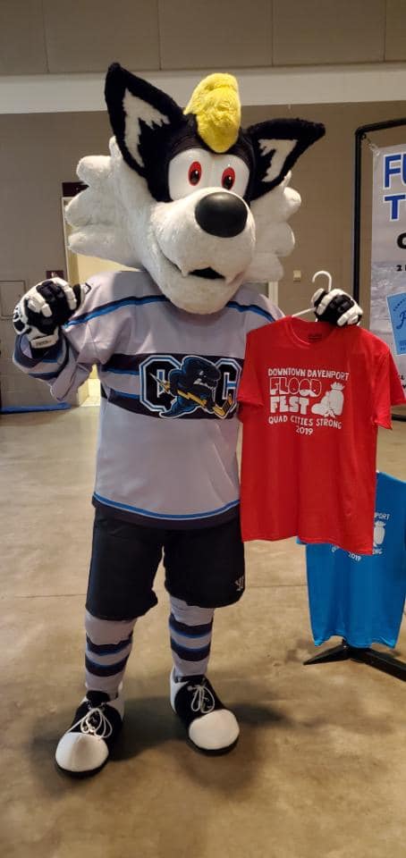 Mascot in costume holding a red T-shirt at community event.