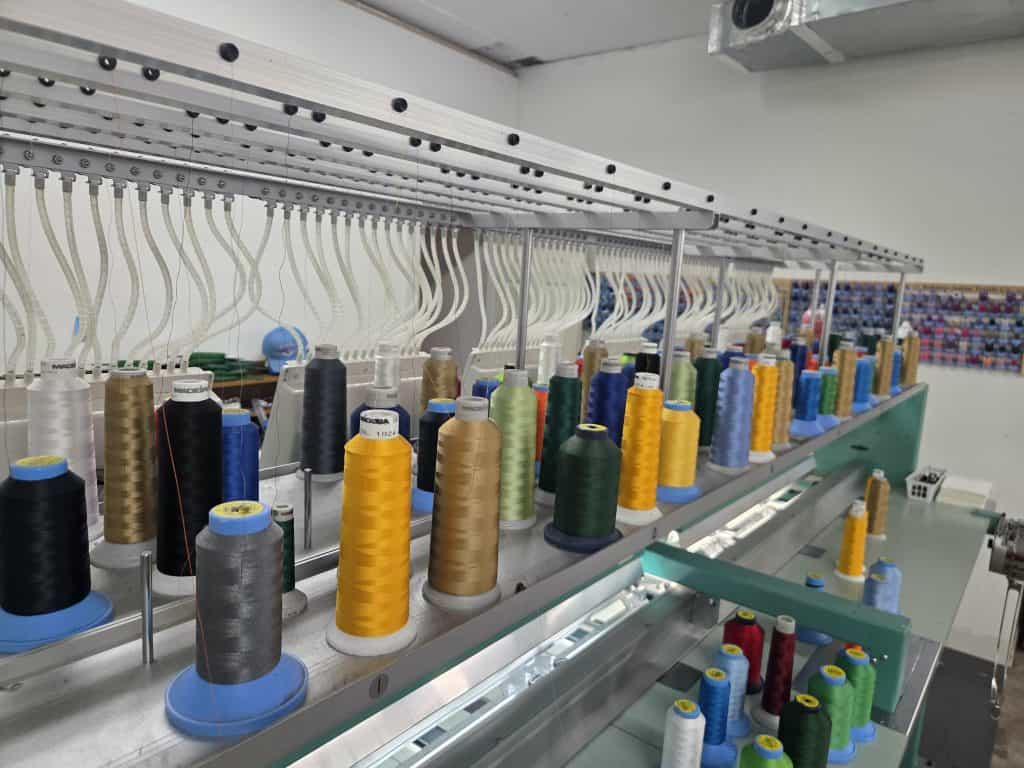 Colorful spools of thread on a sewing machine at QC Custom Tees.