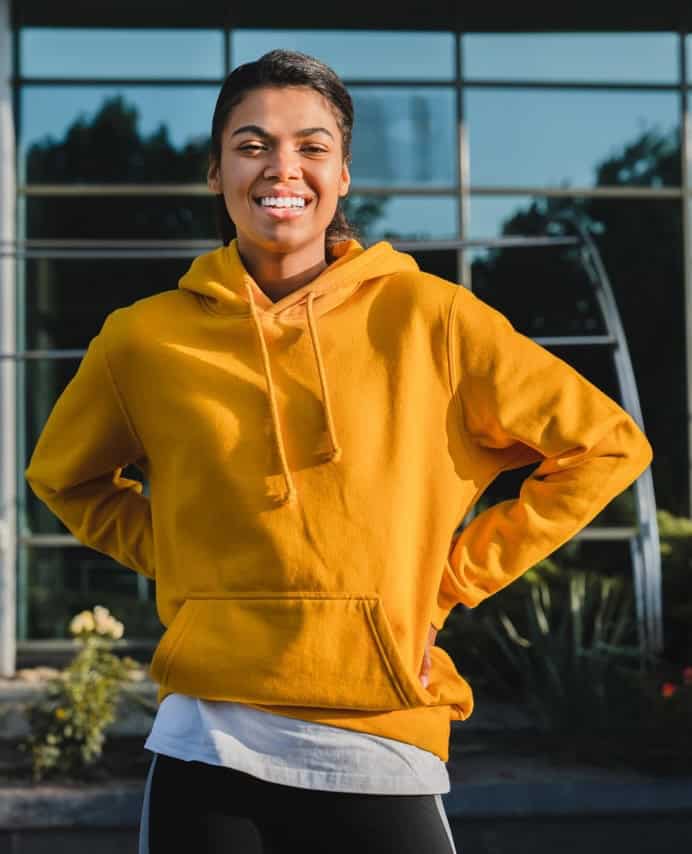 Person wearing a bright yellow hoodie smiling outdoors in front of a modern glass building.